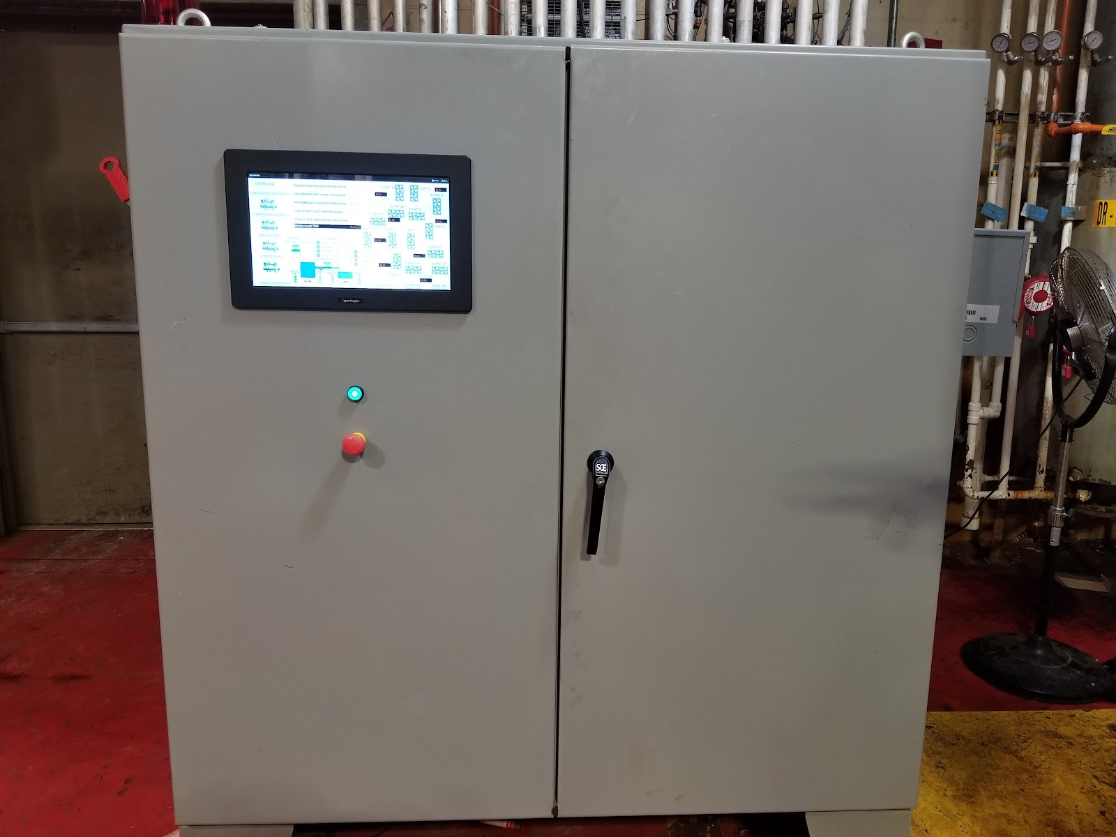 Two-door gray control cabinet on the shop floor with a door-mounted HMI.