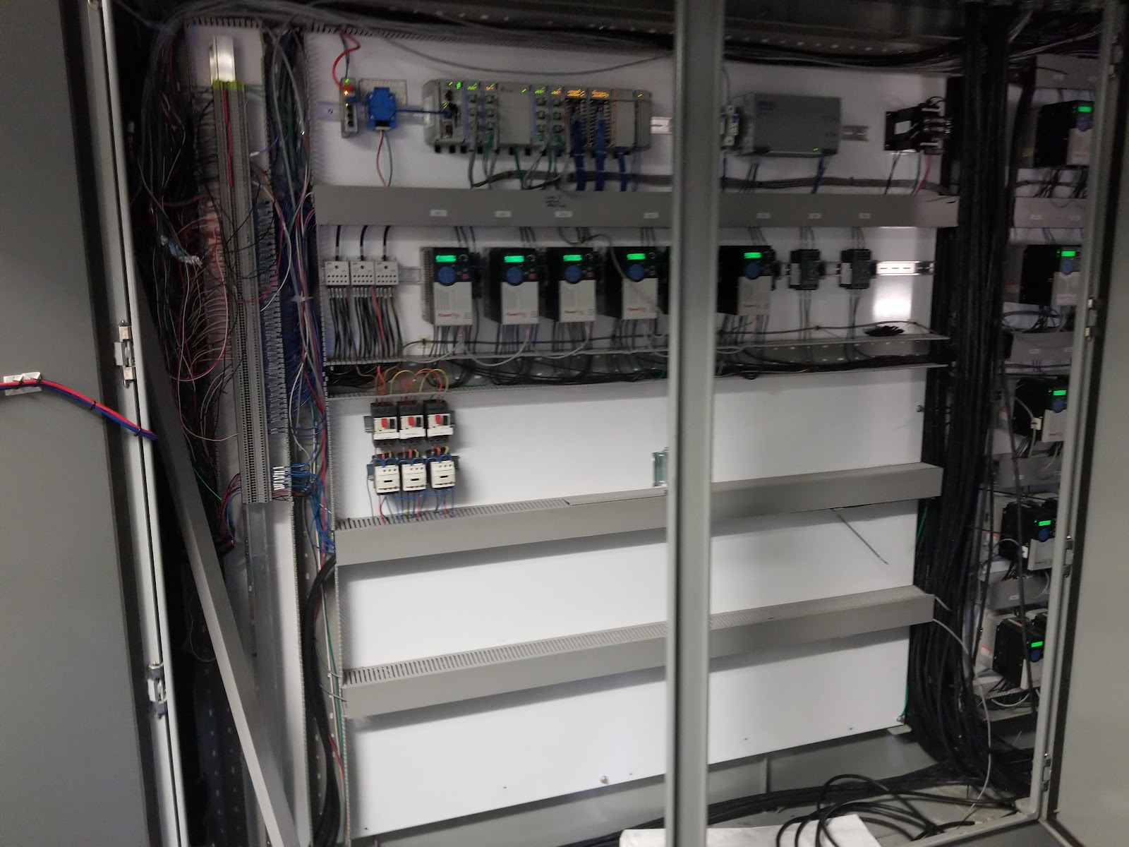 Tall control cabinet interior with stacked DIN rails and modules.