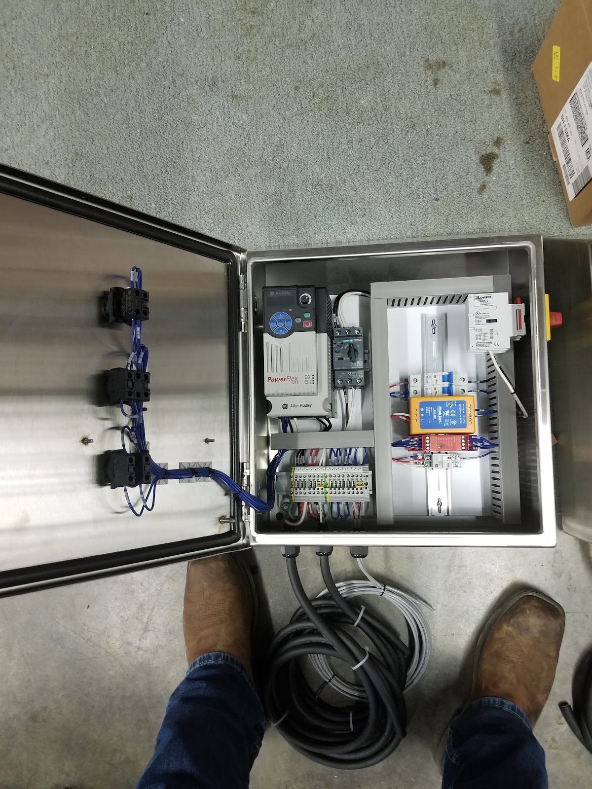 Wall-mounted open panel with PLC, breakers, and door pushbuttons.