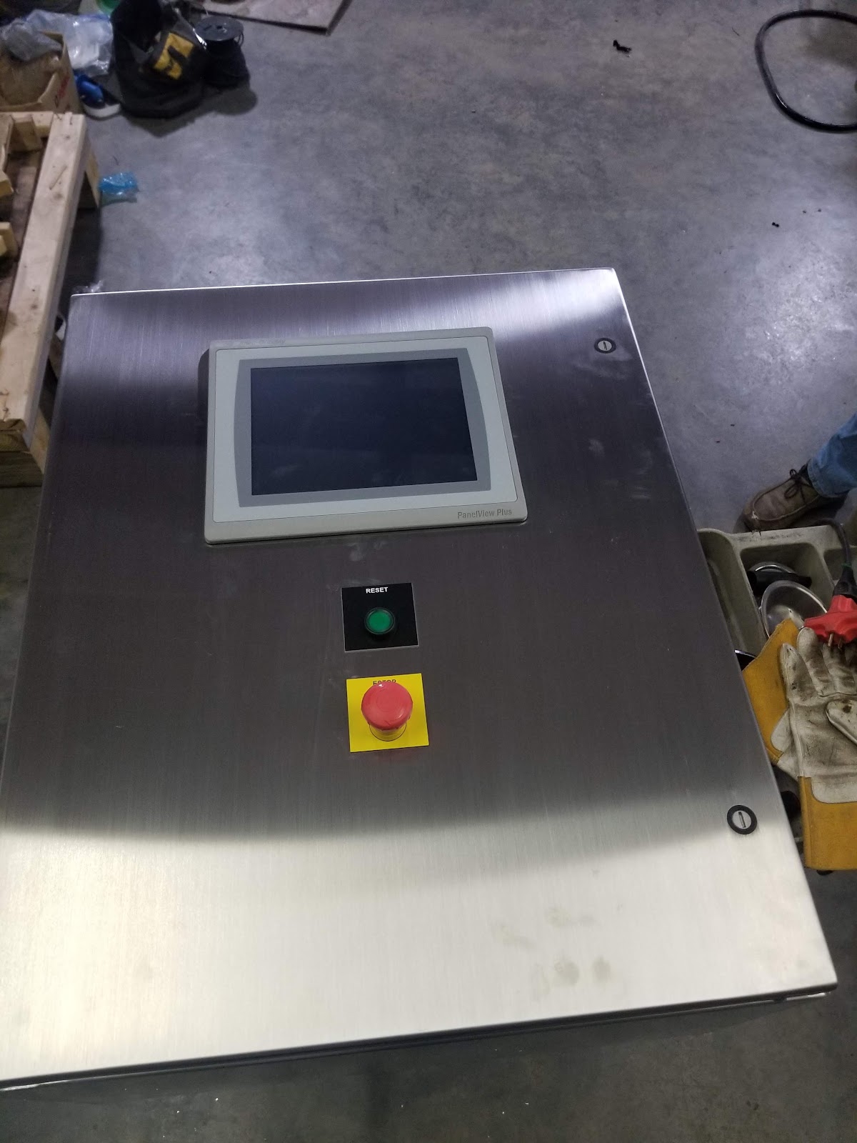 Stainless faceplate on the shop floor with an HMI cutout and emergency stop.