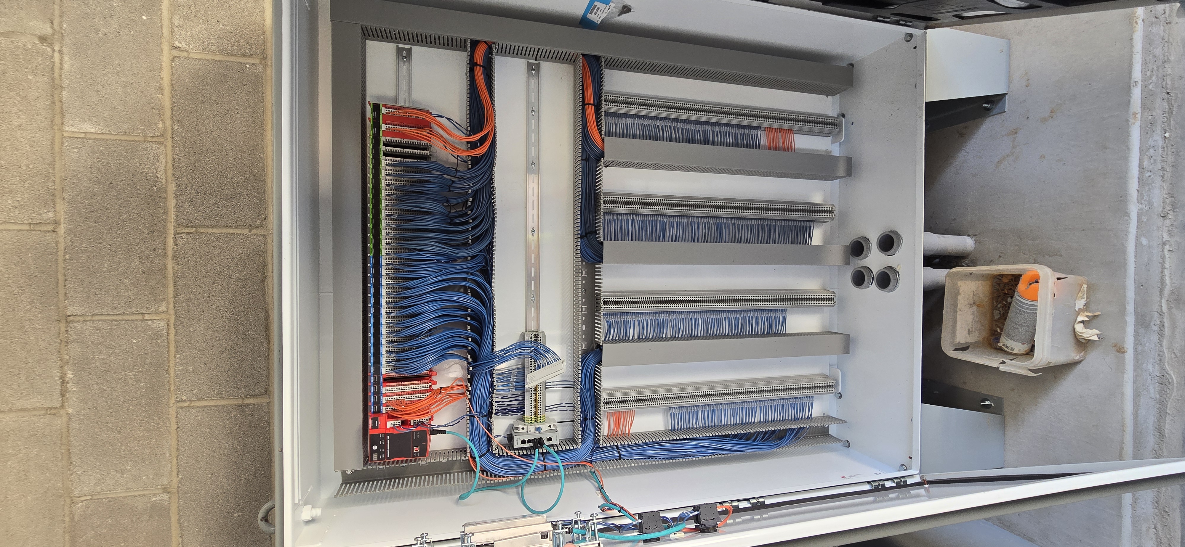 Open control cabinet with PLC I/O, blue field wiring, and wire duct.